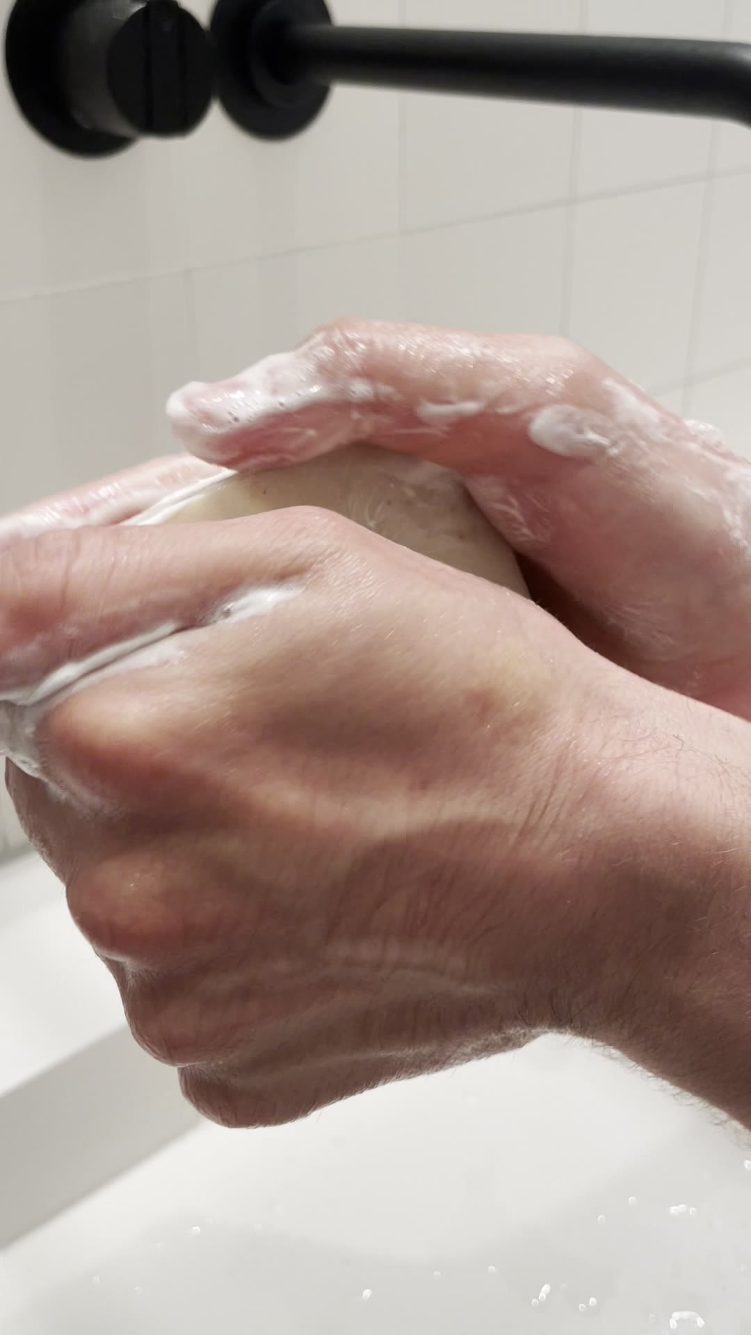 Hände waschen sich mit einem festen Seifenstück am Waschbecken